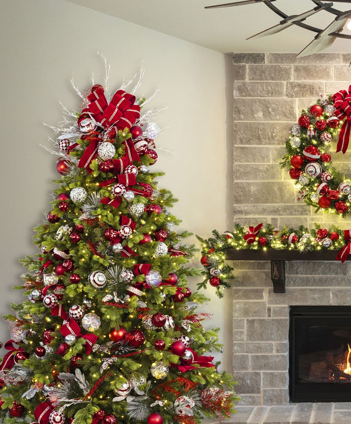 A decorated tree beside a stone fireplace with a matching wreath and mantel garland