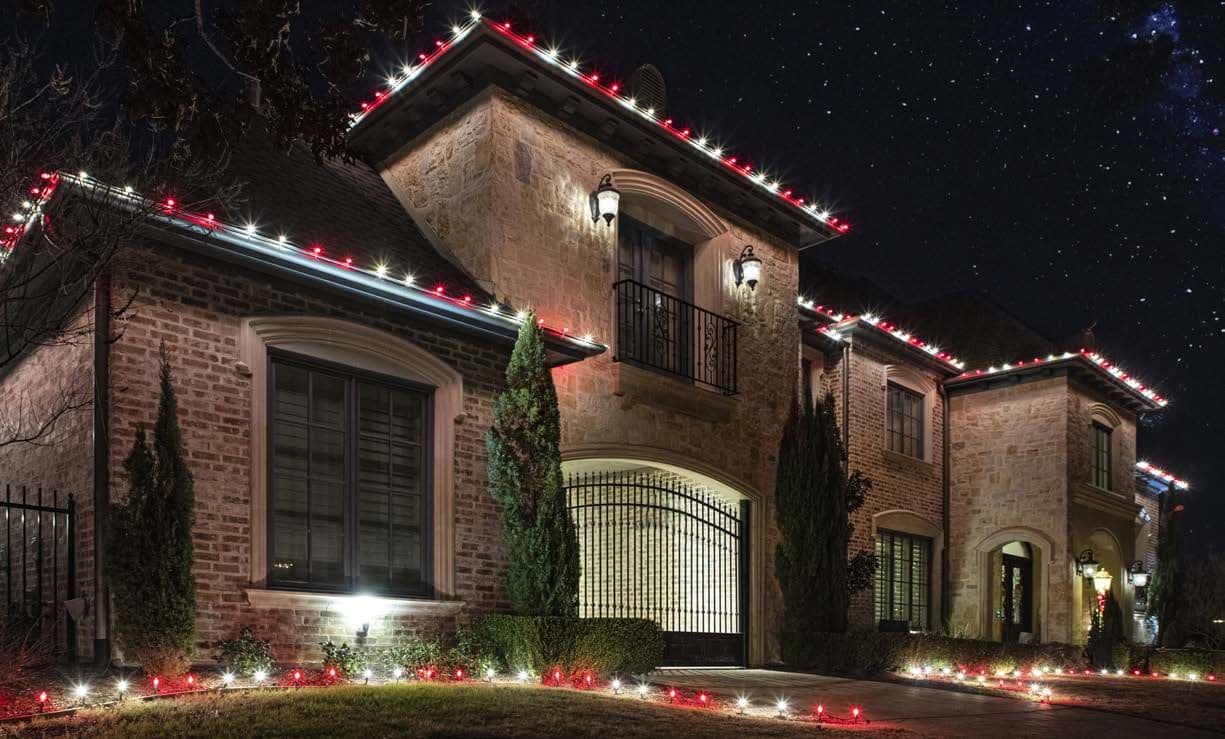 A two-story house with warm white lights along every roofline at dusk